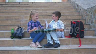 孩子们坐在学校的台阶上，挨着背包，在户外休息时<strong>翻阅</strong>书本