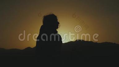 美丽的年轻女子在沙漠中日落时散步的剪影。 穿过沙漠，沙丘，风吹，缓慢