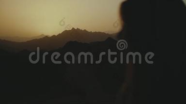 美丽的年轻女子在沙漠中日落时散步的剪影。 穿过沙漠，沙丘，风吹，缓慢