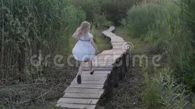 穿着白色连衣裙的<strong>活泼</strong>可爱的小女孩沿着大自然中的木桥在绿色的植被中奔跑