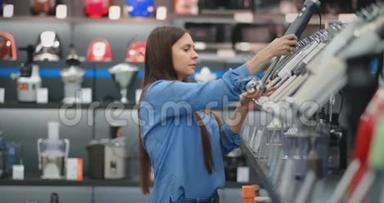 在<strong>电器商店</strong>的厨房用具中，一个穿着蓝色衬衫的黑发女人手里拿着搅拌器