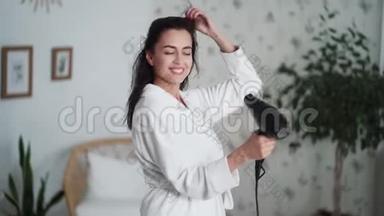 年轻女子穿着白色浴袍跳舞，用吹风机吹干头发