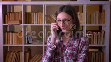 在<strong>室内图</strong>书馆打电话的戴眼镜的年轻漂亮女学生的特写镜头
