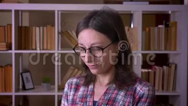 一位戴着眼镜、带着羞涩微笑、看着<strong>图书馆</strong>里摄像机的年轻迷<strong>人</strong>女学生的特写镜头