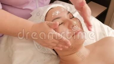 美容师将白色奶油涂在美容院中年亚洲妇女的脸上。 <strong>振兴</strong>、放松和愈合