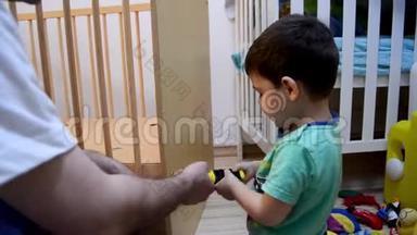 可爱的两岁男孩帮助他的父亲为他的小弟弟放下小床