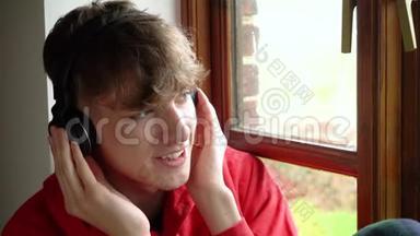 青少年男子坐在窗边听无线蓝牙耳机和手机上的音乐