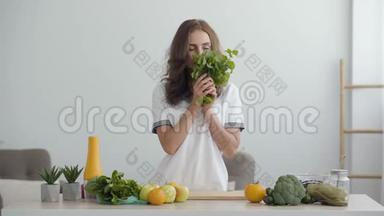 年轻的微笑的女人嗅着站在现代厨房餐桌前的新鲜绿色。 <strong>健康</strong>食品的概念.. <strong>职业</strong>