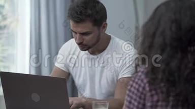 忙碌的胡须男坐在家里的笔记本电脑前工作，而他的妻子对他大喊大叫。 对小玩意的上瘾