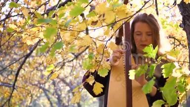一个年轻的女孩弹竖琴。 她坐在秋天公园的一棵树下。
