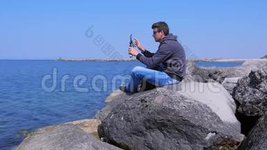 人类<strong>开始</strong>在智能手机上录制<strong>视频</strong>，三脚架坐在大海上的巨大石头上。