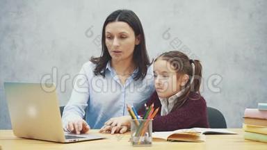 母亲和十几岁的女孩带着笔记本电脑一起在灰色背景上。 在这期间，他们正在看手提电脑