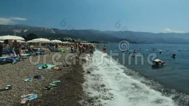 人们游客在度假小镇的鹅卵石海滩上放松。 炎热的夏天度假。 浪打岸上.. 山区