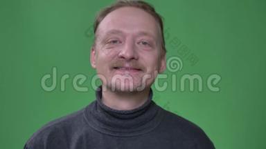 有胡子的金发中年男子的肖像，高兴地看着镜头，在绿色背景上向它眨眼。