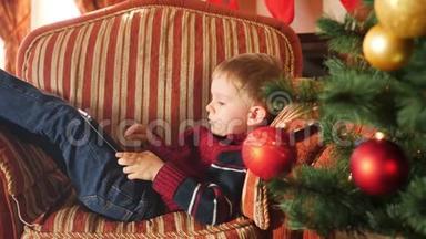 圣诞早晨，小<strong>男孩</strong>躺在扶手椅上，在数码平板电脑上<strong>玩游戏</strong>
