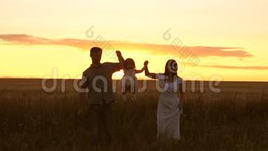 妈妈、宝贝和爸爸正在日落时牵着手走在麦田上。 父亲、女儿和母亲在野外玩耍