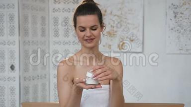 漂亮的黑发女人在白色浴室里打开带有奶油的罐子。