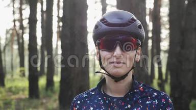 快乐骑自行车女孩拉链在蓝色球衣前，训练前戴黑色头盔和眼镜。 自行车的概念。 慢动作