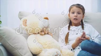 可爱的<strong>小女孩</strong>坐在沙发上，和她的泰迪<strong>说话</strong>，拼命地弯曲她的手指。
