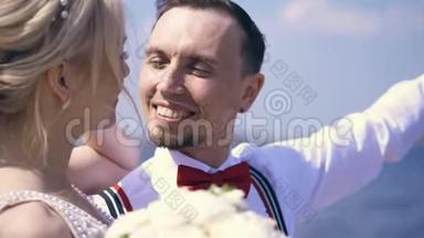 一对漂亮的新婚夫妇。 肖像，新郎看着新娘，微笑着，对着蔚蓝的大海和天空。 夏季