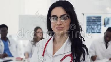 一位戴眼镜的年轻漂亮女医生的画像正看着镜头，她的同事们正在微笑