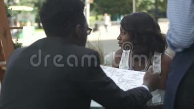 非裔美国人和他的女伴坐在外面的咖啡馆里点餐