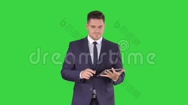商人在他的平板电脑上走来走去，看着摄像机在绿色上呈现一些东西
