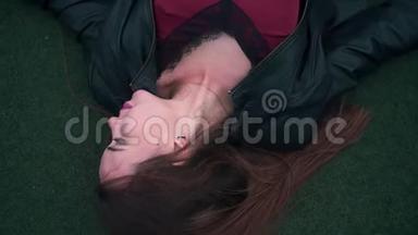 一个美丽而热情的女孩躺在法庭的地板上。 一个年轻的女人躺在球场的绿色表面上。