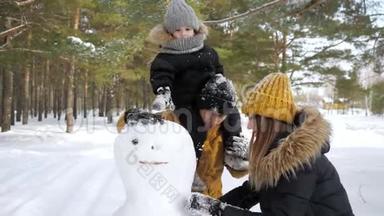 年轻的家庭，妈妈，儿子和爸爸正在冬季城市公园堆雪人。