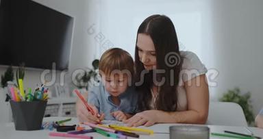 一家人有一个孩子，一个男孩和一个年轻的母亲坐在桌子旁，用彩色<strong>铅笔</strong>在纸上<strong>画画</strong>。 发展