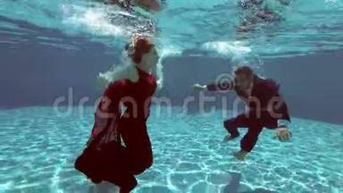 穿着红色裙子的新娘和穿着西装的新郎在游泳池里水下游泳，摄影师带他们去对抗