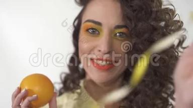 特写年轻顽皮的微笑女孩的肖像，明亮的化妆，拿着橙色和玩丝带。 慢动作。