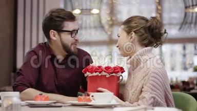 年轻夫妇坐在餐厅的桌子旁，女人亲吻男人拿着花