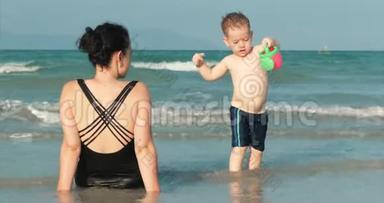 快乐和无忧无虑的母子在海边玩耍，晒日光浴，游泳。 儿童和成人在热带海域玩耍