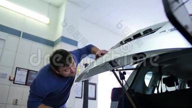 无油漆凹痕修复。 一个穿蓝色套头衫的人在一家汽车修理厂修理后备箱。 修补无油漆的凹痕