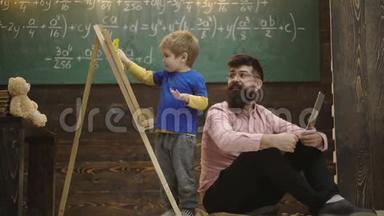 <strong>微笑的老师</strong>戴着眼镜看着孩子擦拭黑板。 父亲和兴奋<strong>的</strong>金发孩子学习数学。 侧视男孩和
