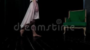 一个穿着三文鱼色连衣裙的女孩走在一个带绿色椅子的黑暗房间里。