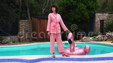 泳池附近穿着粉红色睡衣的年轻模特女孩接触粉红色的火烈鸟