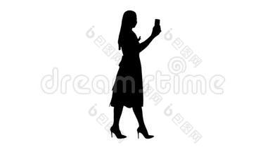 年轻女子穿着粉红色的手拿着用智能手机<strong>录制</strong>视频博客边走。