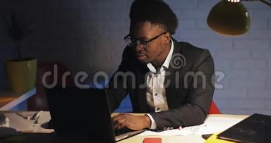 年轻的商人深夜在办公室里用笔记本电脑工作。 他读了好消息，完成了工作。