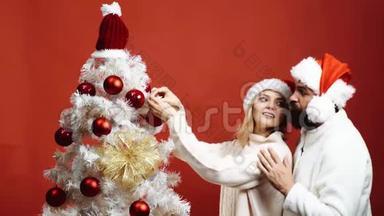 戴红帽子的长胡子男人拥抱一个<strong>装饰圣诞树</strong>的女人。 可爱的夫妇<strong>装饰圣诞树</strong>