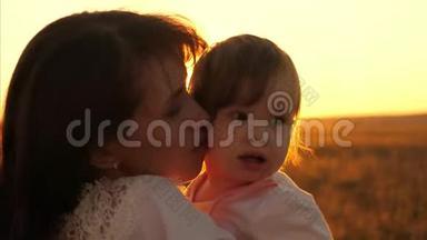 <strong>妈妈</strong>把她的小女儿抱在<strong>怀里</strong>。 欢乐的一家人在公园温暖的夏日傍晚看日落