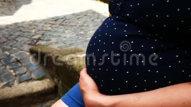 孕妇坐着，穿着圆点<strong>孕妇装</strong>，用手抚摸着肚子