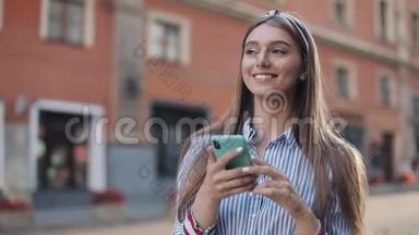 微笑的年轻女子穿着蓝色和白色条纹连衣裙，用智能手机在老街上走来走去