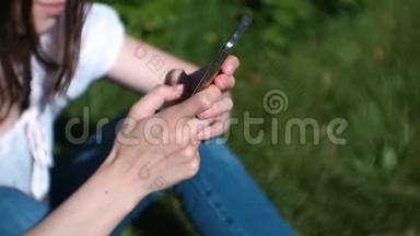 女人在阳光明媚的日子里坐在公园里，聊天，在手机上输入一条信息。 双手特写..