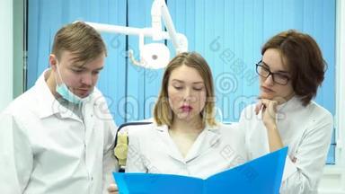 医生在蓝色文件夹里翻阅病历，摇头，坏消息和医学概念。 三个年轻人
