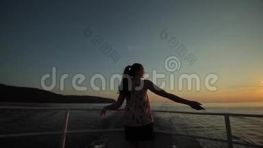 一个美丽的女孩站在风中，对抗日落的天空，河流和山脉。 背面