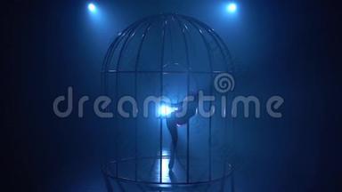 一个女孩在笼子里的舞台上抱箍旋转的剪影。 蓝色烟雾背景。 剪影。 慢动作