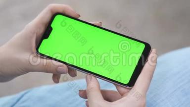 女孩水平地拿着一部智能手机，在屏幕上观看视频。 追踪绿色屏幕智能手机