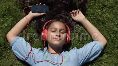 在阳光明媚的天气里，一个留着长发的小女孩躺在公园里，用耳机听音乐。 4K